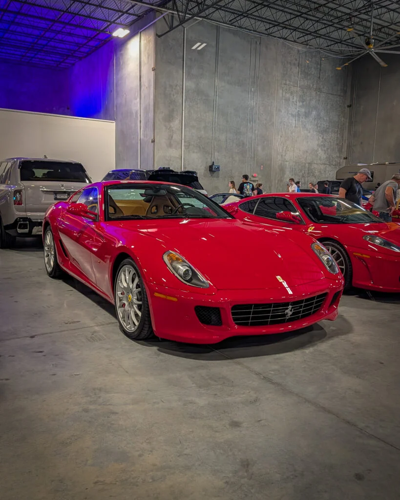 Two red Ferraris parked indoors with people and other vehicles in the background