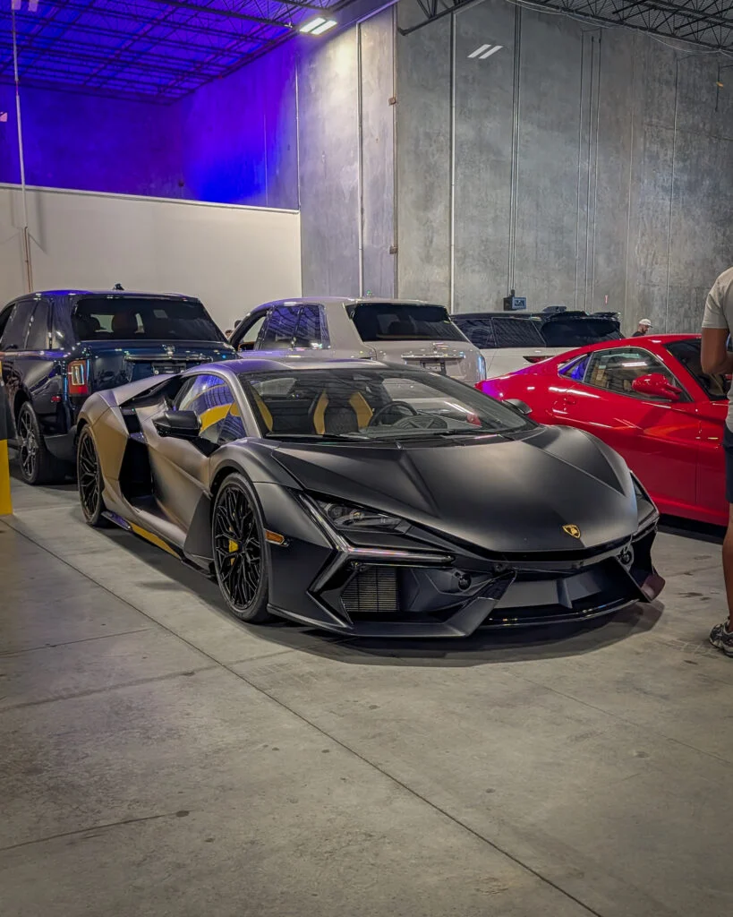 Matte black Lamborghini Revuelto with yellow interior parked indoors along with other SUVs and a red car