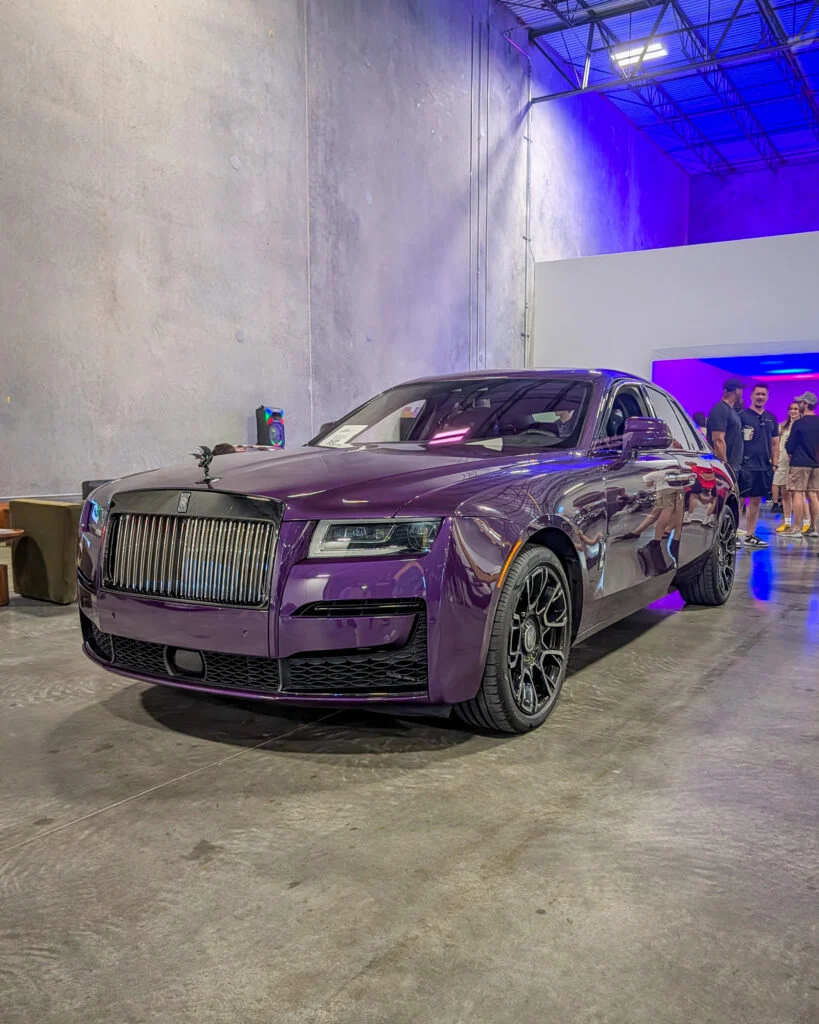 Purple Rolls-Royce sedan parked indoors with people in the background under blue lighting