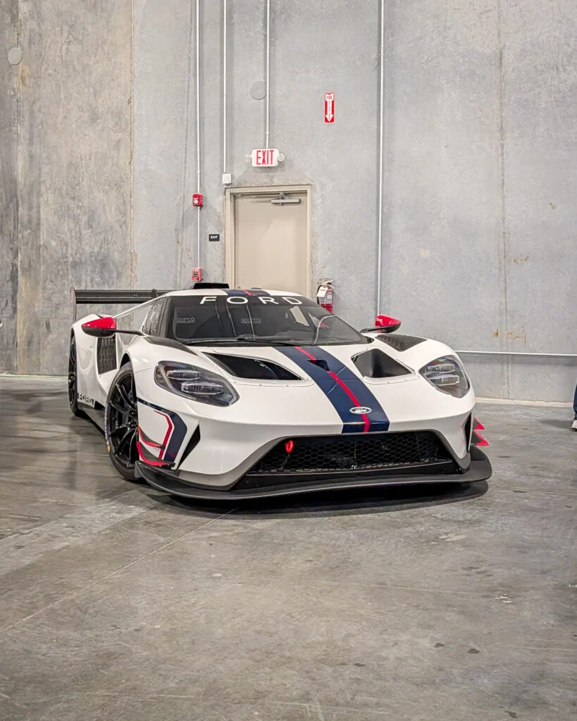 White Ford GT race car with blue and red stripes parked indoors near an exit door