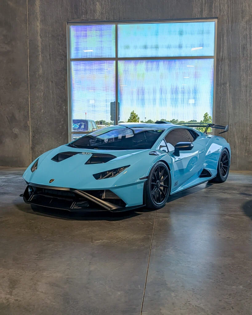 Light blue Lamborghini Huracán STO parked indoors near a large window with concrete walls and floor