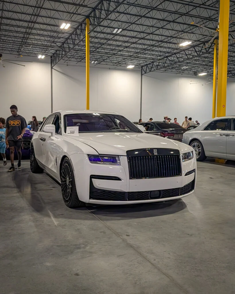 White Rolls-Royce Ghost parked indoors with several people and other cars in the background
