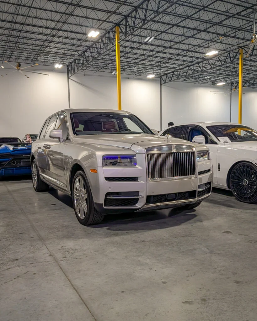 Silver Rolls-Royce SUV and white Rolls-Royce sedan parked indoors under ceiling fans and lights