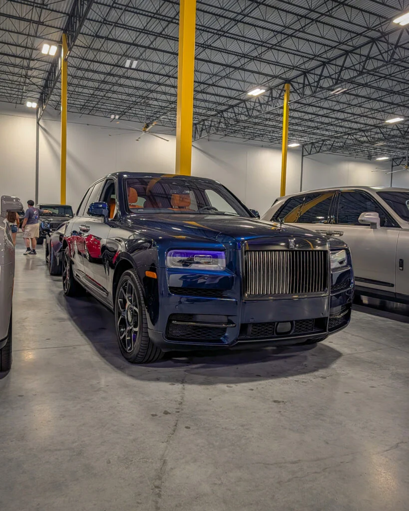Dark blue Rolls-Royce SUV in an indoor showroom with yellow pillars and other vehicles in the background