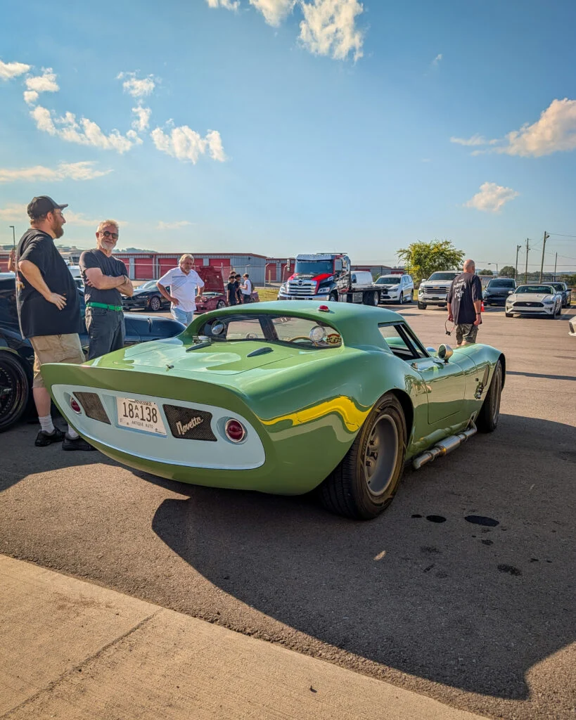 Green Novetta coupe parked outdoors with people standing nearby and other vehicles in background under a clear sky.