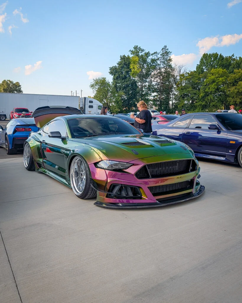 Chameleon green Mustang parked outdoors with people and other cars around on a clear day