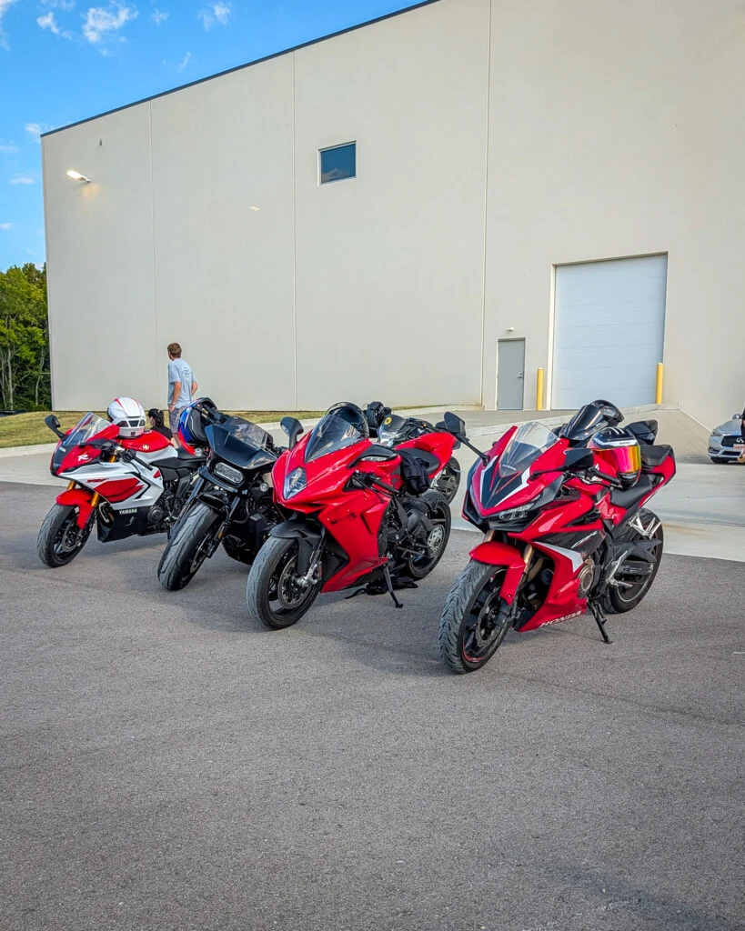 Three red sport motorcycles and one black motorcycle parked outside a beige building with two people standing nearby under a