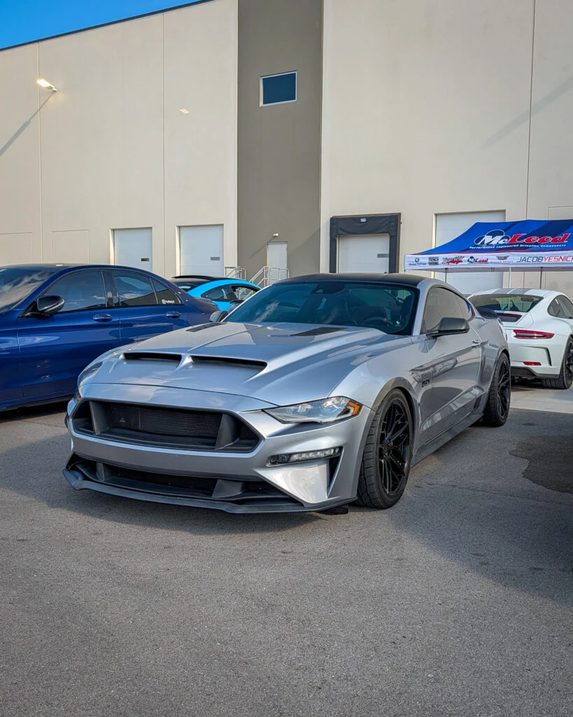 Silver Ford Mustang GT parked outside a building with other vehicles visible nearby