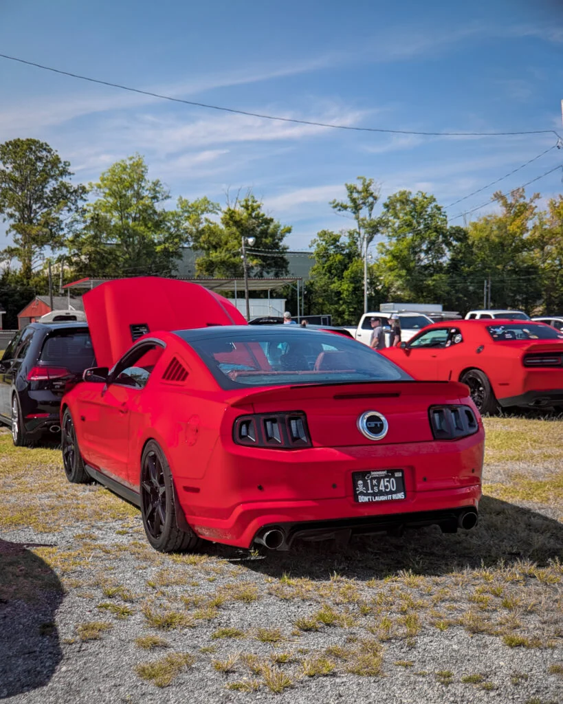 Red Ford Mustang GT with hood open in parking area at car event on a clear day