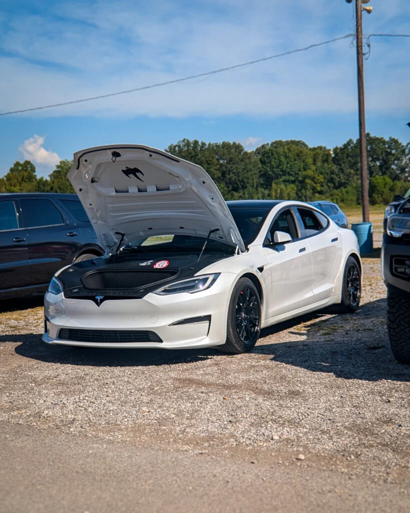 White Tesla Model S with hood open in a parking lot on a clear day