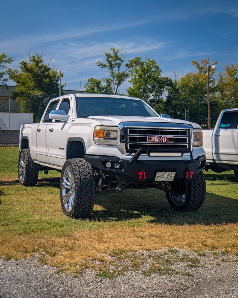 White GMC Sierra pickup truck parked on grass with trees and a building in the background on a clear day
