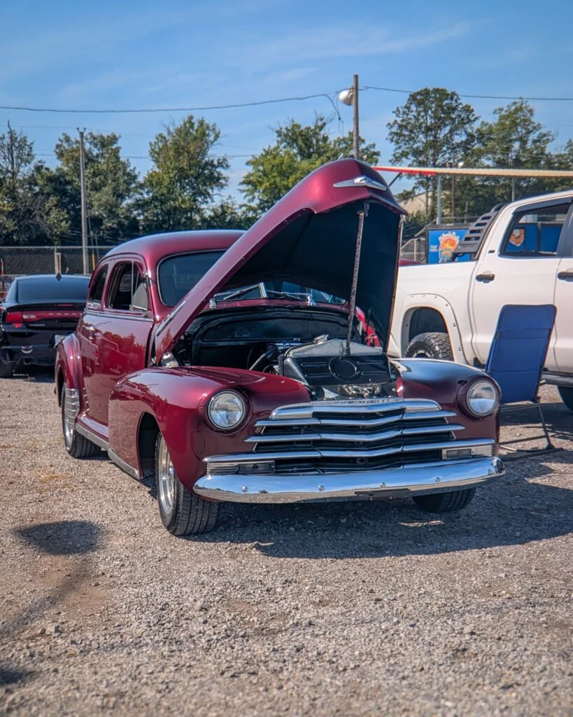 Maroon Chevrolet Fleetmaster with hood open in a parking lot during a car event