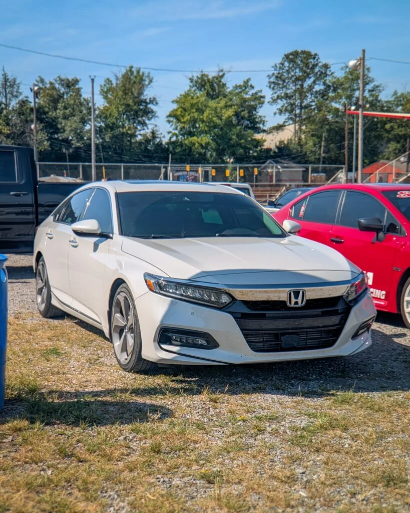 White Honda Accord parked on gravel lot with other cars and trees in background