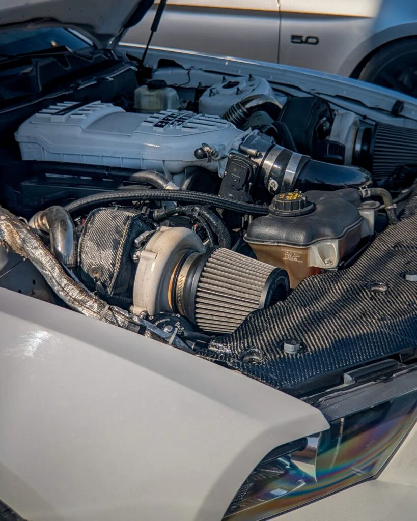 Close-up of a white Ford Mustang 5.0 engine bay at a car event
