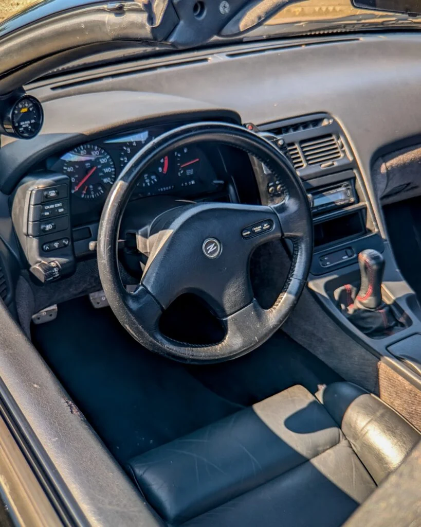 Black Nissan 300ZX steering wheel and dashboard with manual shifter, photographed from the driver's side