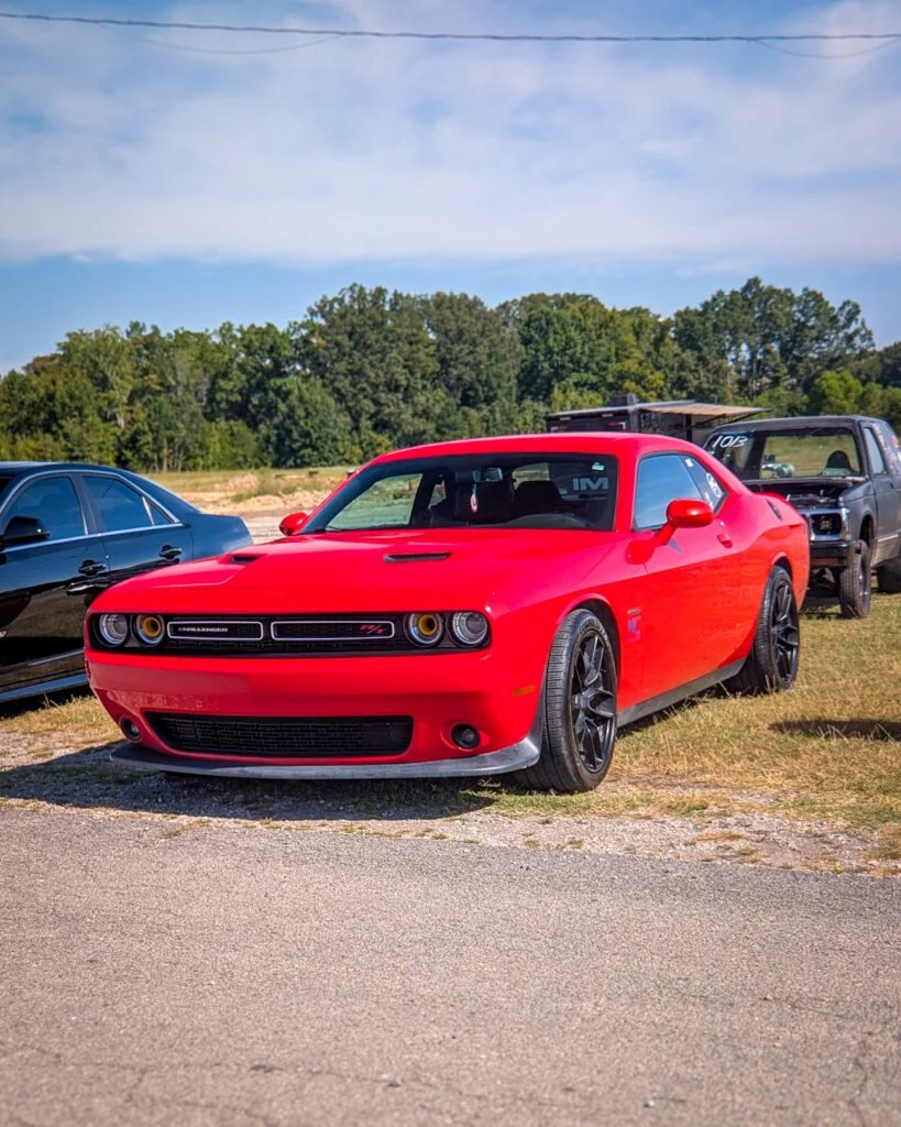 Red Dodge Challenger R/T parked outdoors near other vehicles under blue sky with trees in background