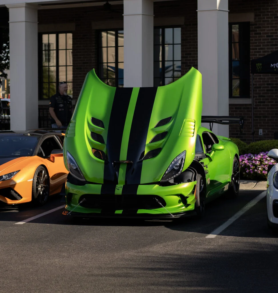 Bright green Dodge Viper with black racing stripes and raised hood at an outdoor car event parking lot