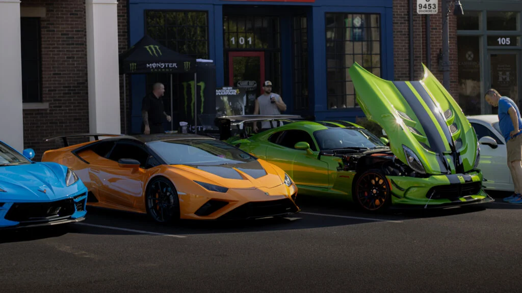 Blue Chevrolet Corvette, orange Lamborghini Huracan, and green Dodge Viper with hood open parked in front of brick building a