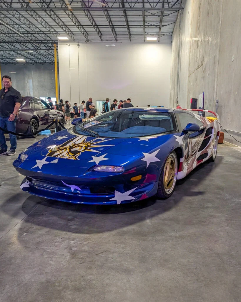 Vector M12 American Anthem parked indoors with people and another dark vehicle in background