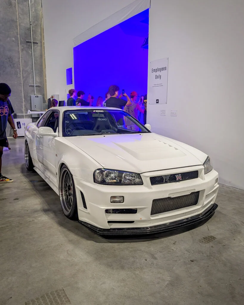 White Nissan Skyline GT-R parked indoors with people in the background near a blue-lit area