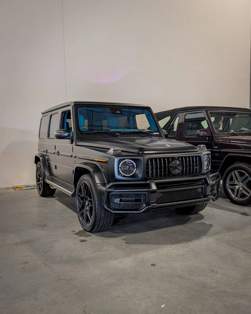 Black Mercedes-Benz G-Class SUV parked indoors next to a dark purple Mercedes-Benz convertible