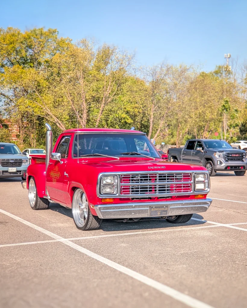 Red Dodge pickup truck parked in a lot with trees in the background under clear sky.