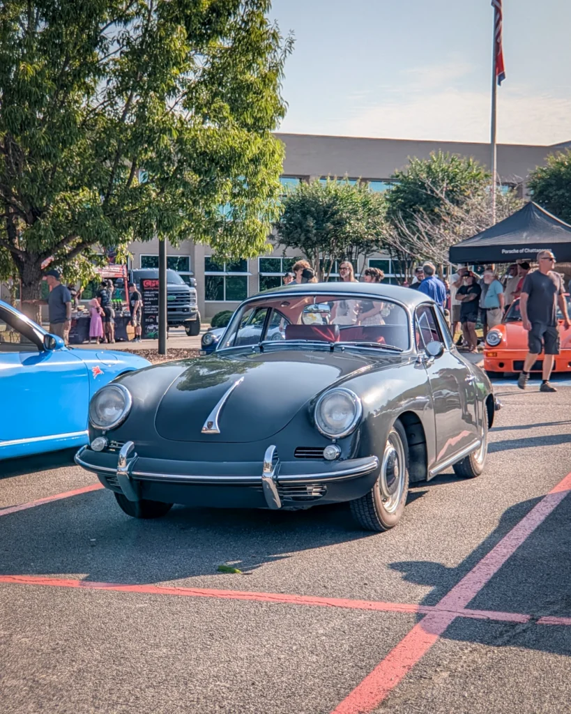 Gray Porsche 356 parked at a car meet with people and tents in the background on a sunny day.