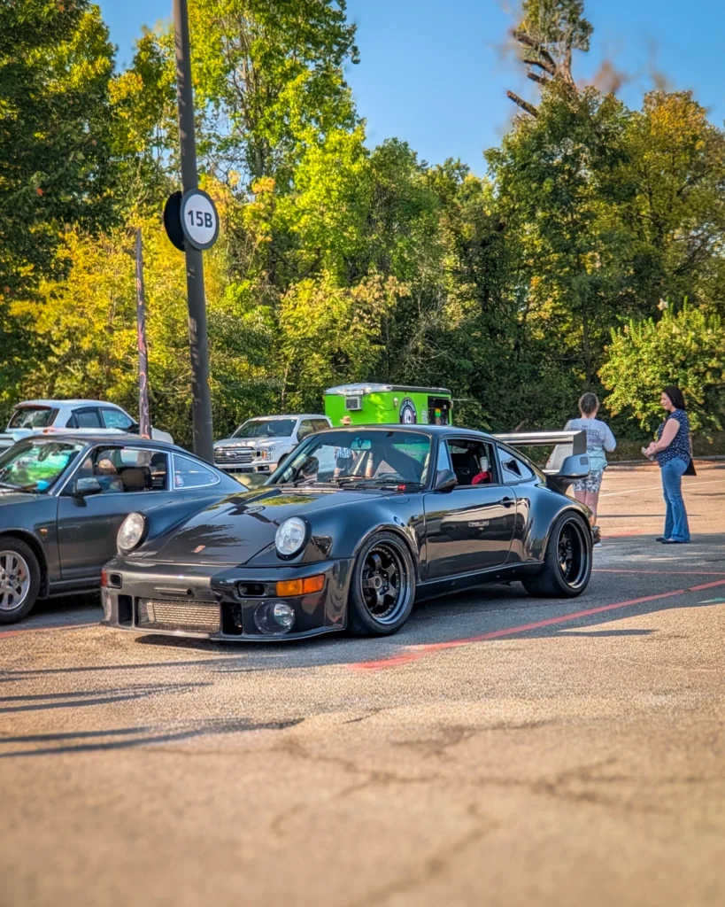 Black Porsche 911 with large rear wing parked in a lot with people and trees in the background