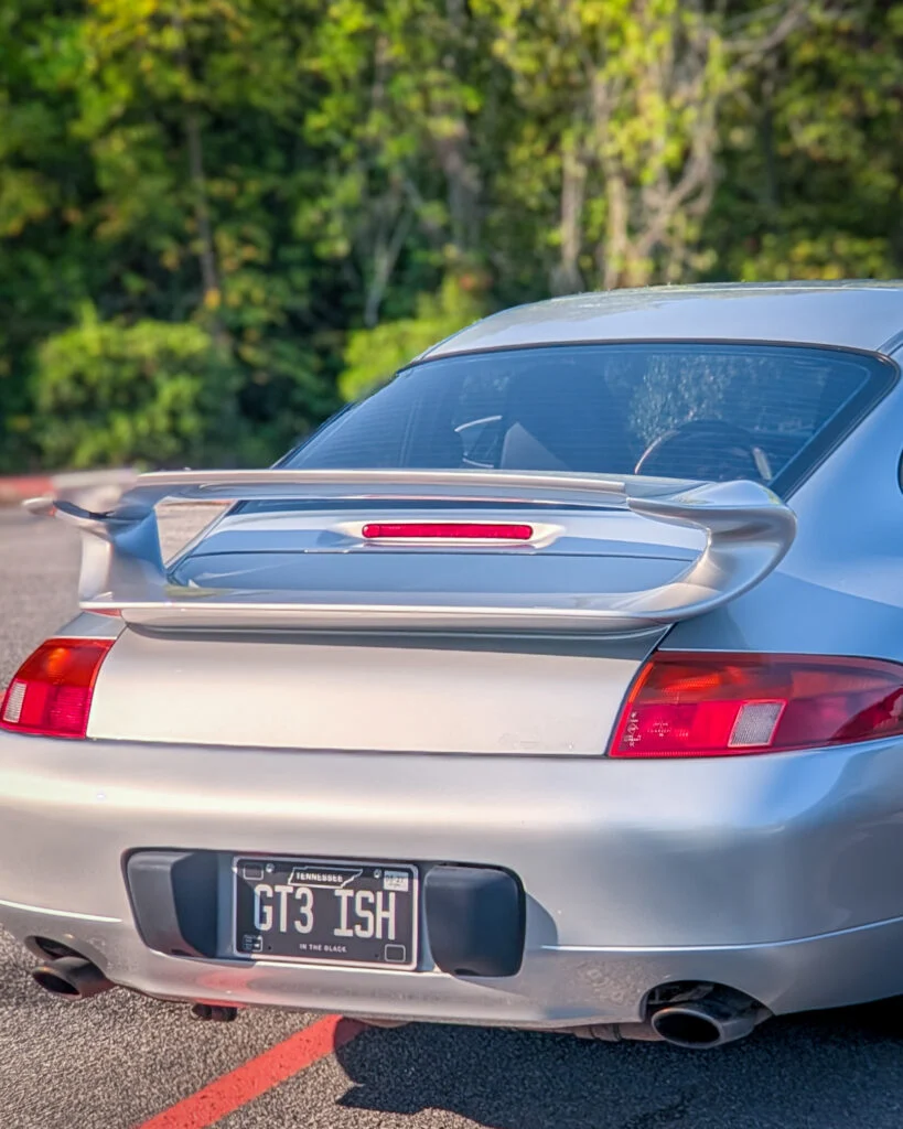 Silver Porsche 911 with rear wing and Tennessee license plate parked outdoors with trees in background