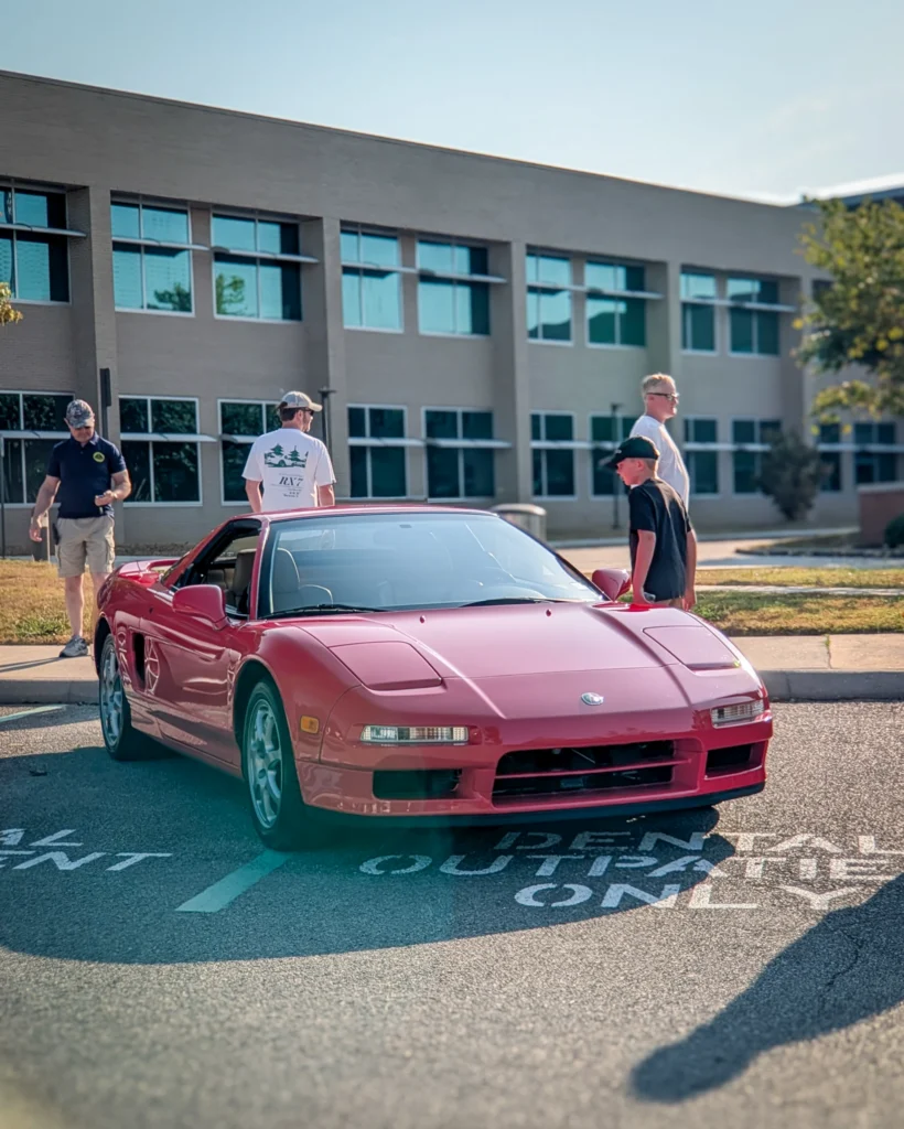 Red Acura NSX parked outside near building with four people nearby on a sunny day