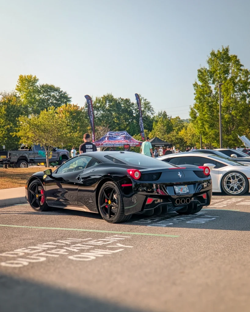 Black Ferrari 458 Italia parked with other cars at an outdoor car event on a sunny day