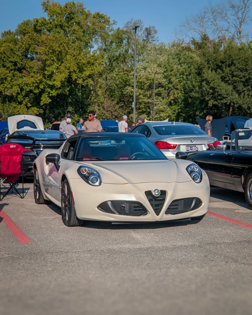 White Alfa Romeo 4C parked in a lot with people and other cars in the background on a clear day