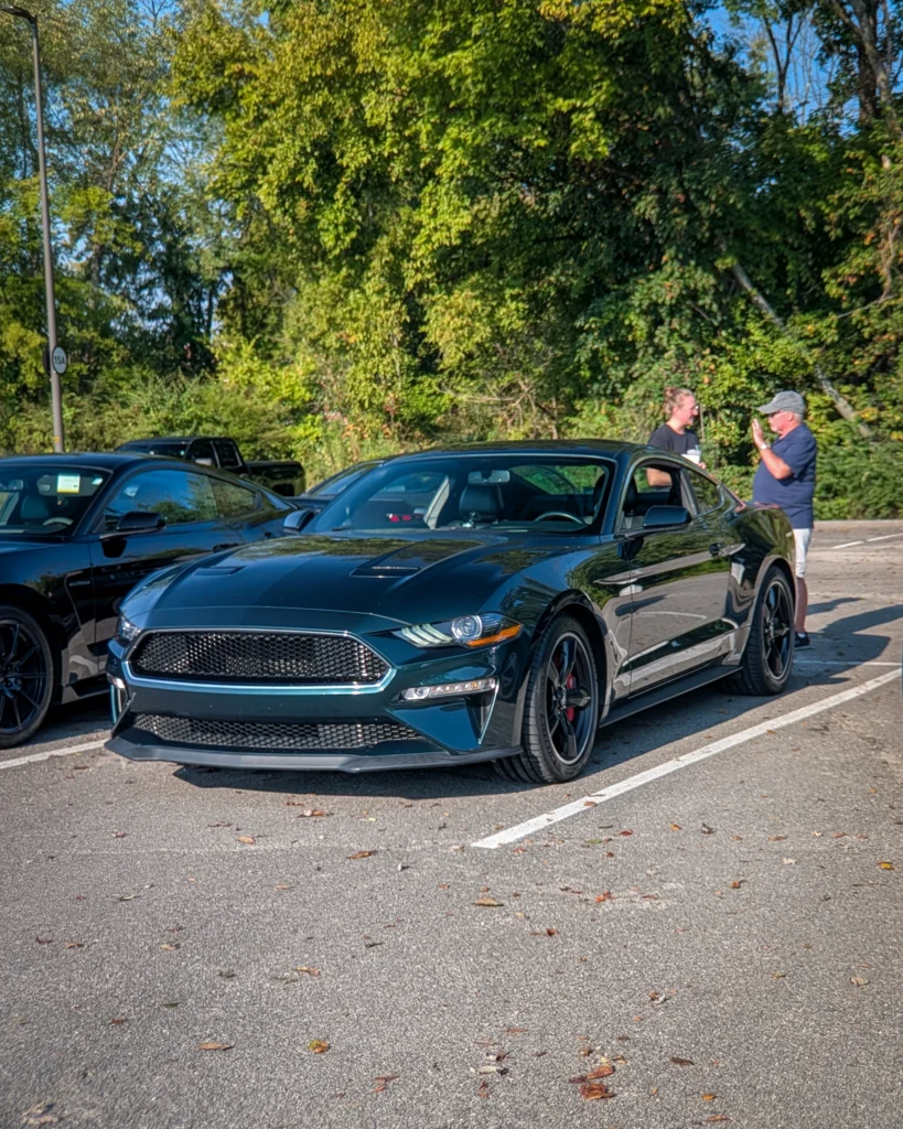 Dark blue Ford Mustang parked at an outdoor car meet with two people standing near the driver’s side of the car.