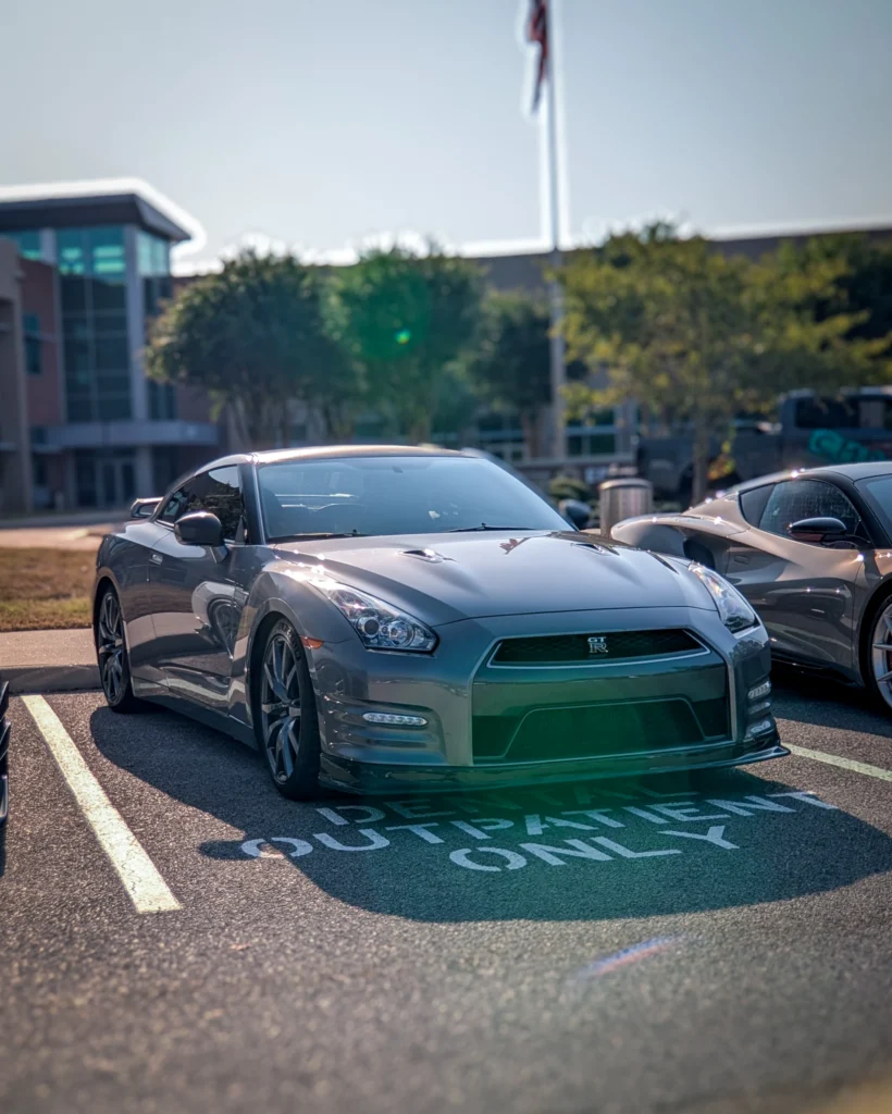 Gray Nissan GT-R parked in a lot with trees and a building in the background