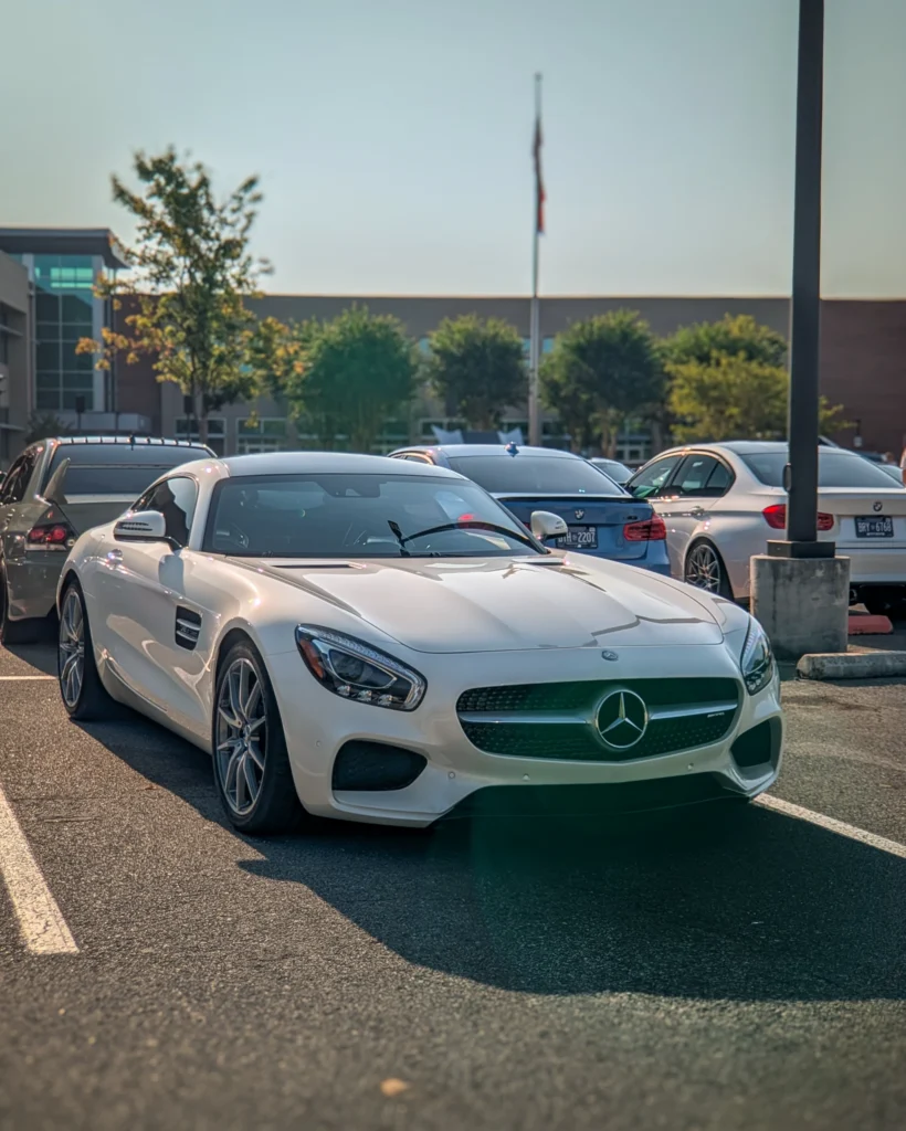 A white Mercedes-Benz AMG GT coupe is parked among other cars in an outdoor parking lot.
