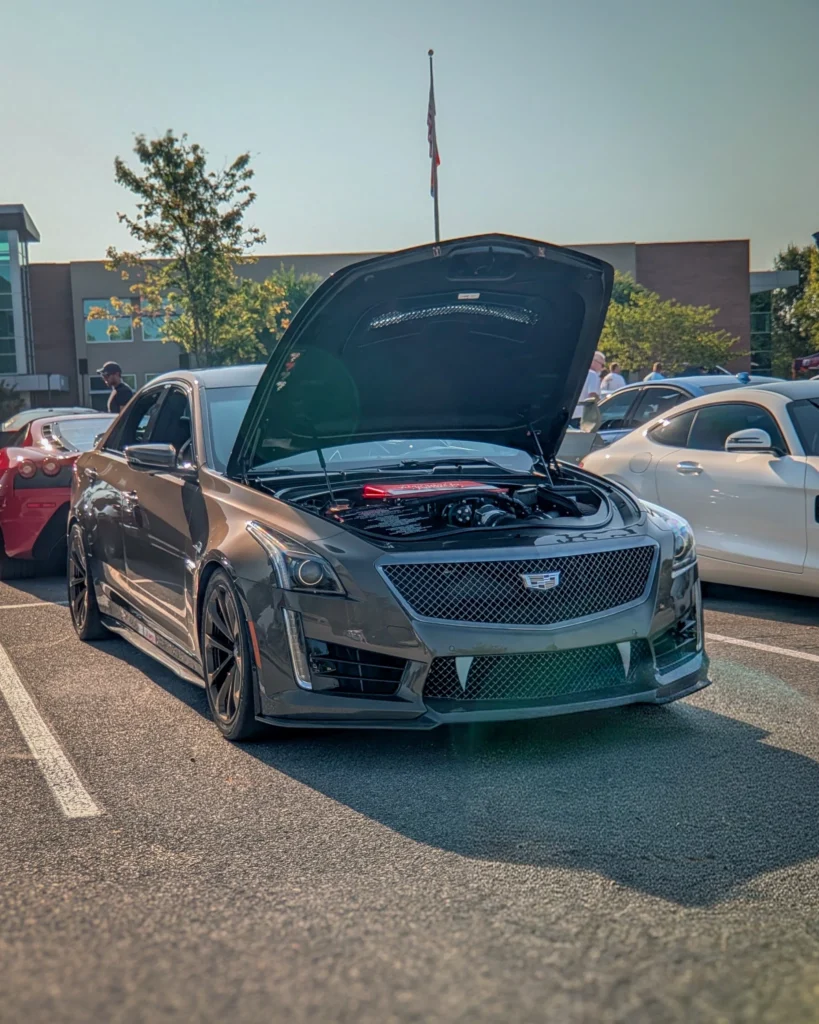 Gray Cadillac CTS-V with hood open in a parking lot at a car event under clear sky