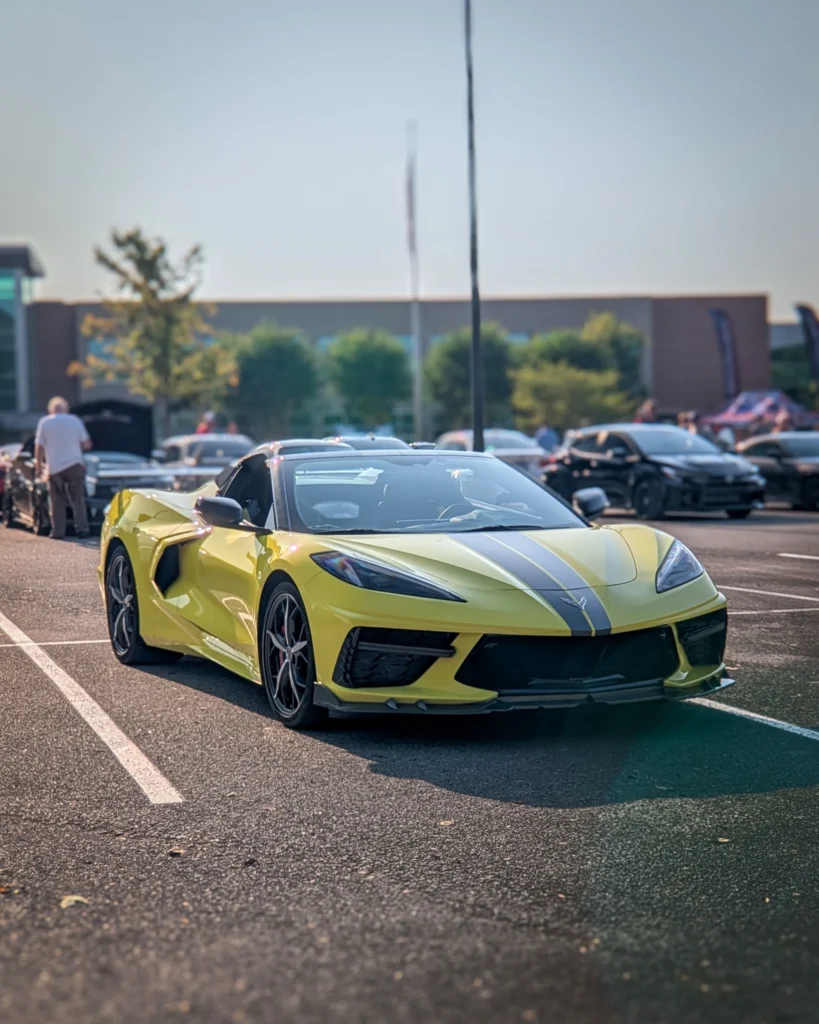 Yellow Chevrolet Corvette convertible with black racing stripes parked at a car event in a parking lot