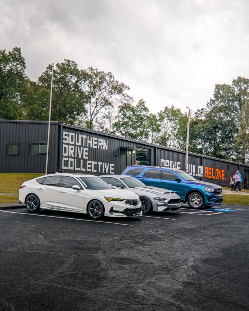 White Acura Integra, gray Ford Mustang, and blue Dodge Durango SUV parked outside a black building