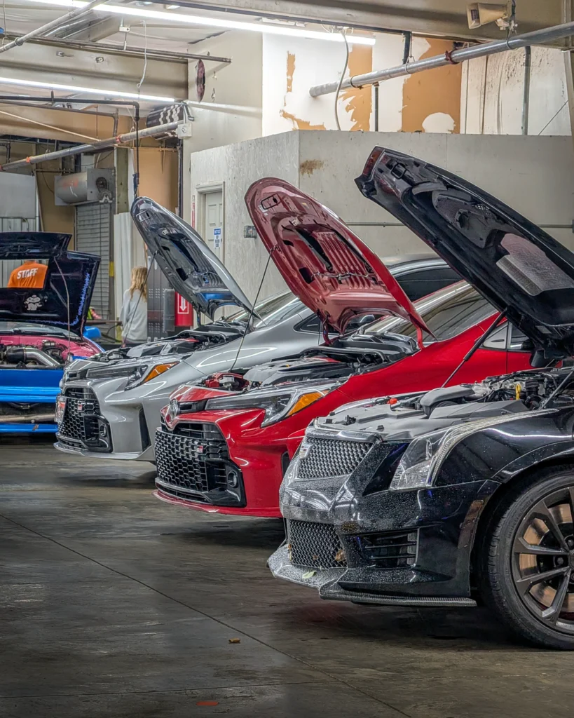 Four cars with open hoods parked indoors showing front and engine compartments in a garage or workshop setting.