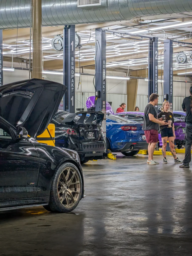 Black Cadillac CTS-V with open hood in a garage with multiple people standing near other cars and lifts