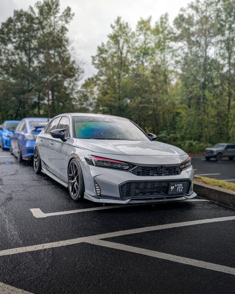 Silver Honda Civic parked in a lot on a rainy day with trees and other vehicles in the background