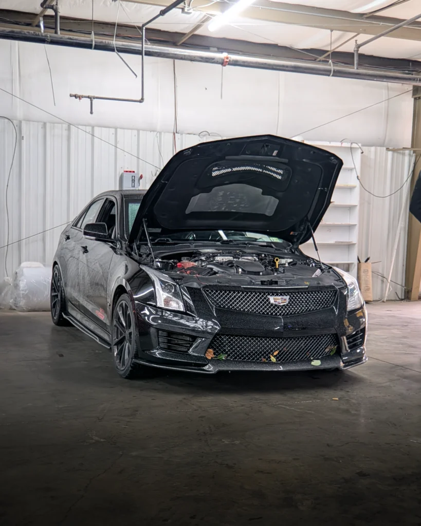 Black Cadillac ATS-V sedan with open hood inside a garage