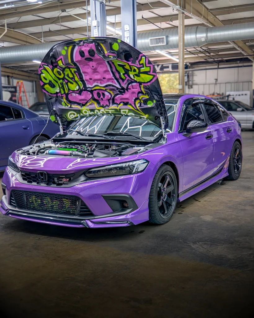 Purple Honda Civic Si with hood open showing graffiti on underside in an indoor garage setting