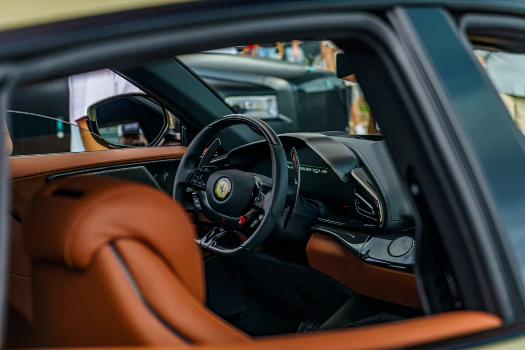 Interior view through open window of a Ferrari with tan leather seats and visible steering wheel and dashboard showing