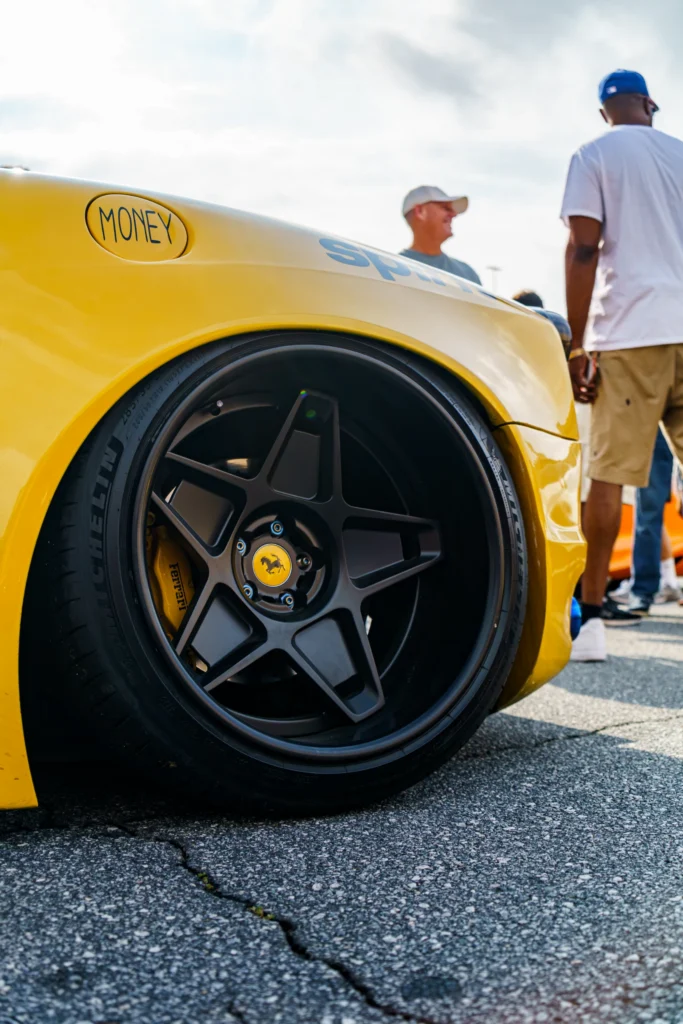 Close-up of yellow Ferrari F430 wheel and tire with two men standing nearby outdoors