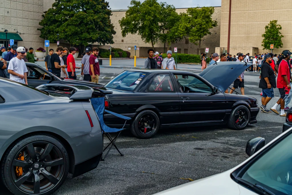 Black Nissan Sentra parked with hood open at car meet, surrounded by people and other vehicles in parking lot