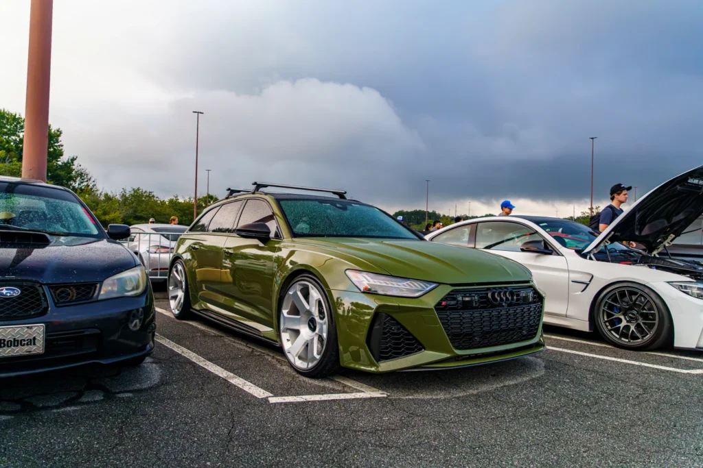 Green Audi RS6 Avant in parking lot with other cars and people under cloudy sky