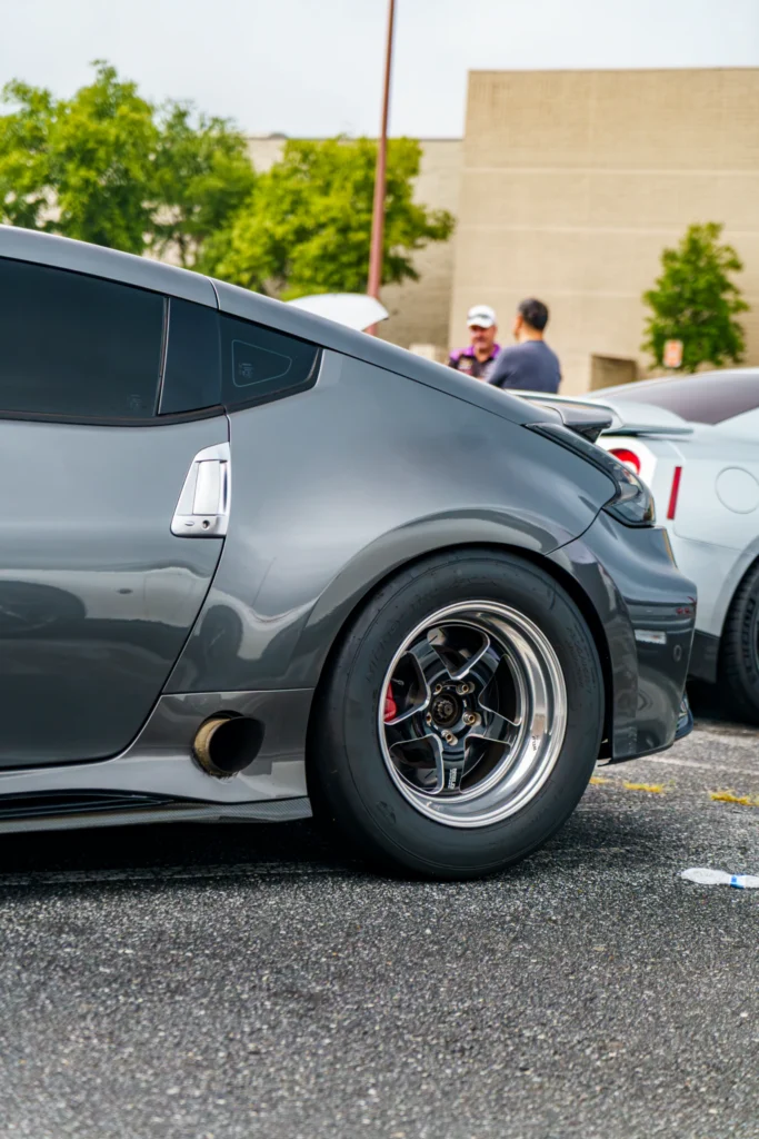 Gray Nissan 370Z with aftermarket wheels and visible rear quarter panel, parked outdoors near a white Nissan GT-R and two