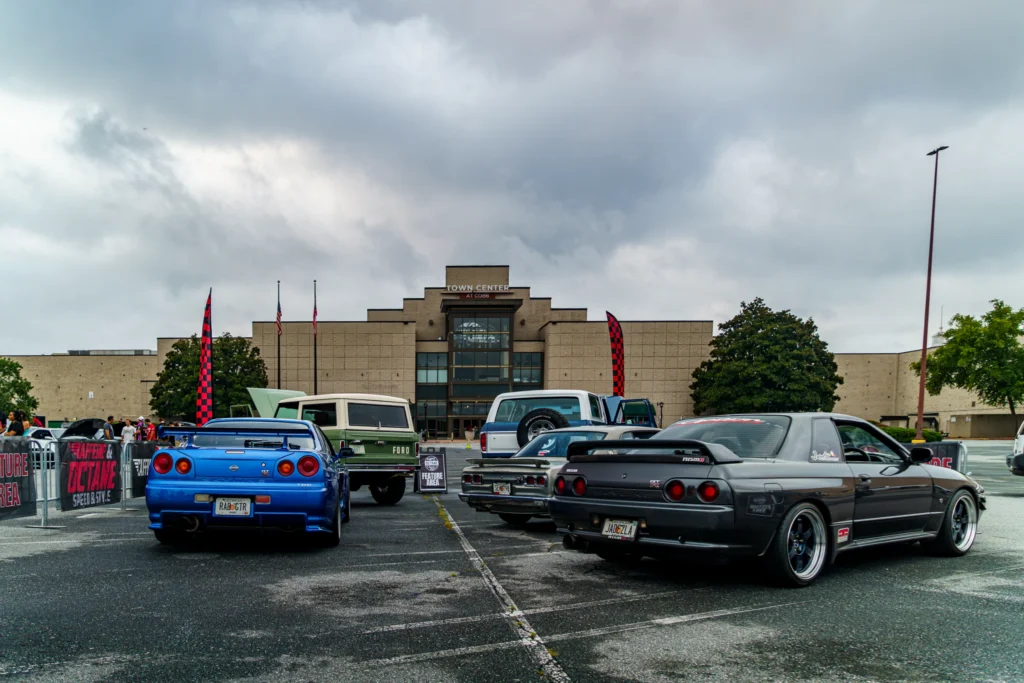 Rear view of multiple cars, including a blue Nissan Skyline and a gray Nissan Skyline, in a parking lot at Town Center at
