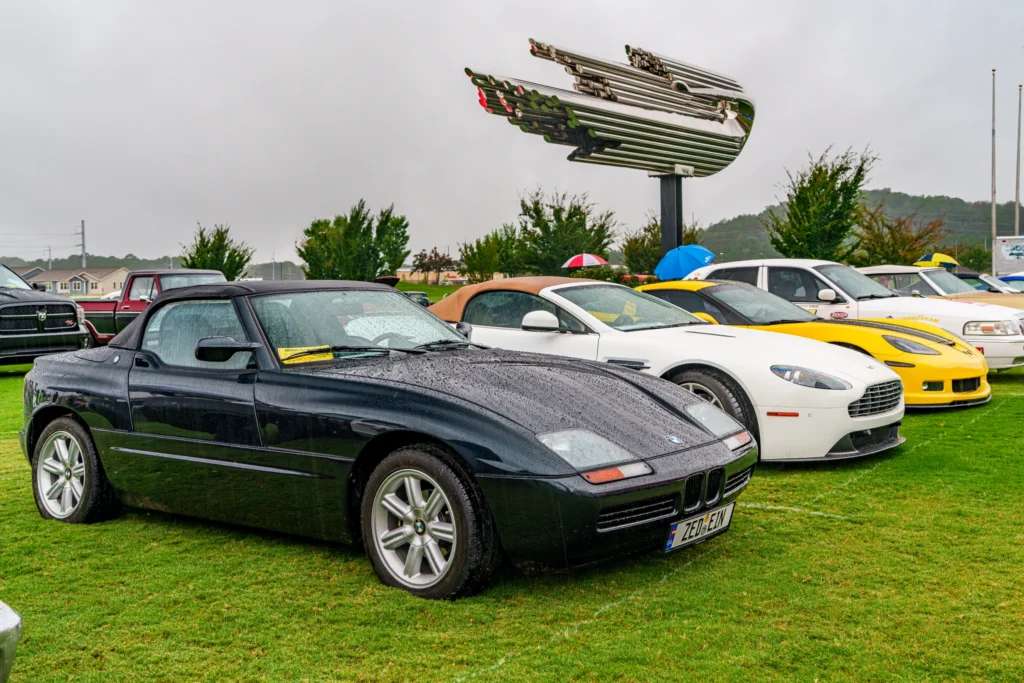 Black BMW Z1 convertible, white Aston Martin V8 Vantage convertible, and yellow Chevrolet Corvette coupe parked on grass